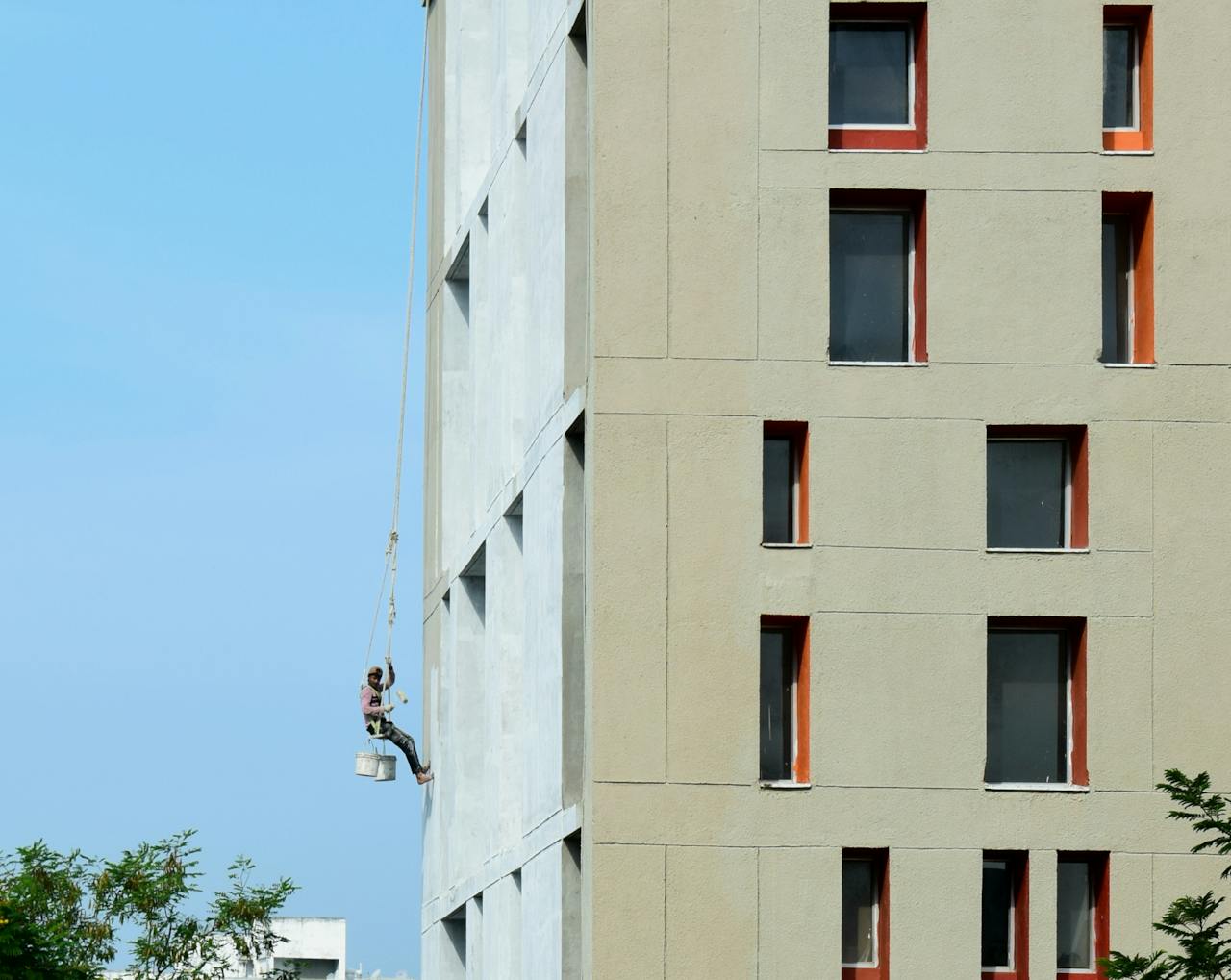 A painter suspended on a building facade, painting a high-rise structure.